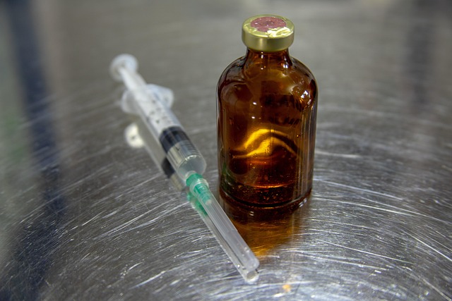 A glass medication vial and a syringe on a metal surface